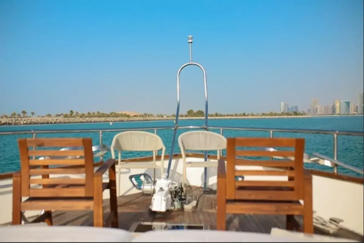 Bow of the 62 Ft Tecno Yacht with wooden and rope chairs, looking across calm water toward the Abu Dhabi skyline