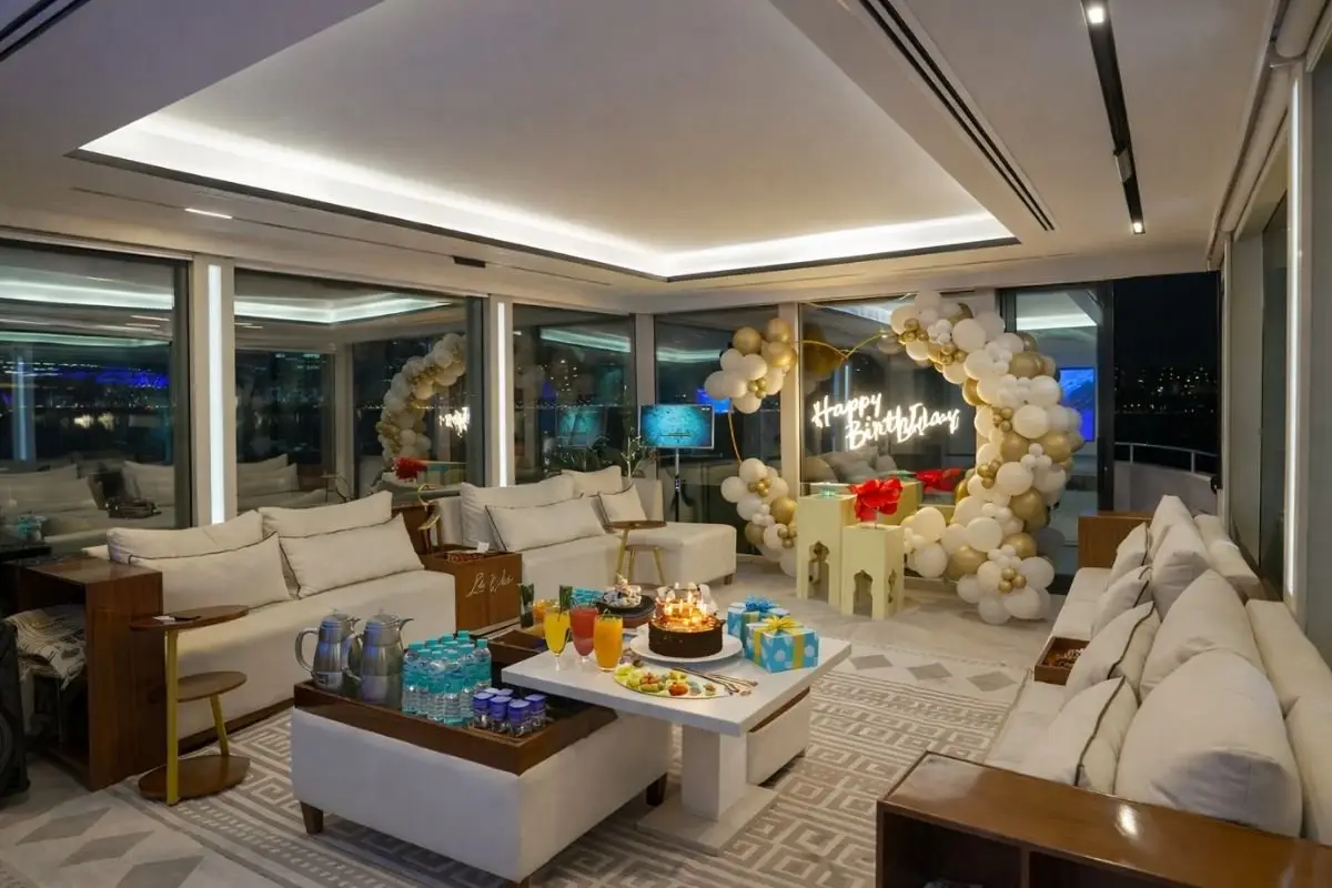 Indoor lounge of the Lavy Luxury Yacht at night with white sofas, a coffee service tray and a decorated corner with a neon sign